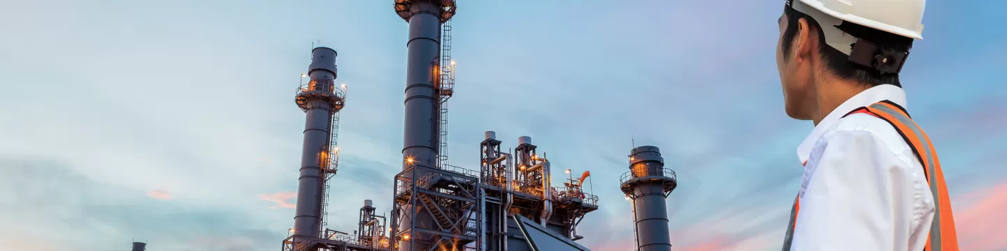 Engineer with notebook standing in front of oil refinery building structure in heavy petrochemical industry